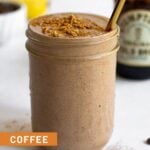 Coffee protein smoothie in a jar with some toppings on it and a straw in it. Around it is a jar of cold brew, coffee beans, and bananas.
