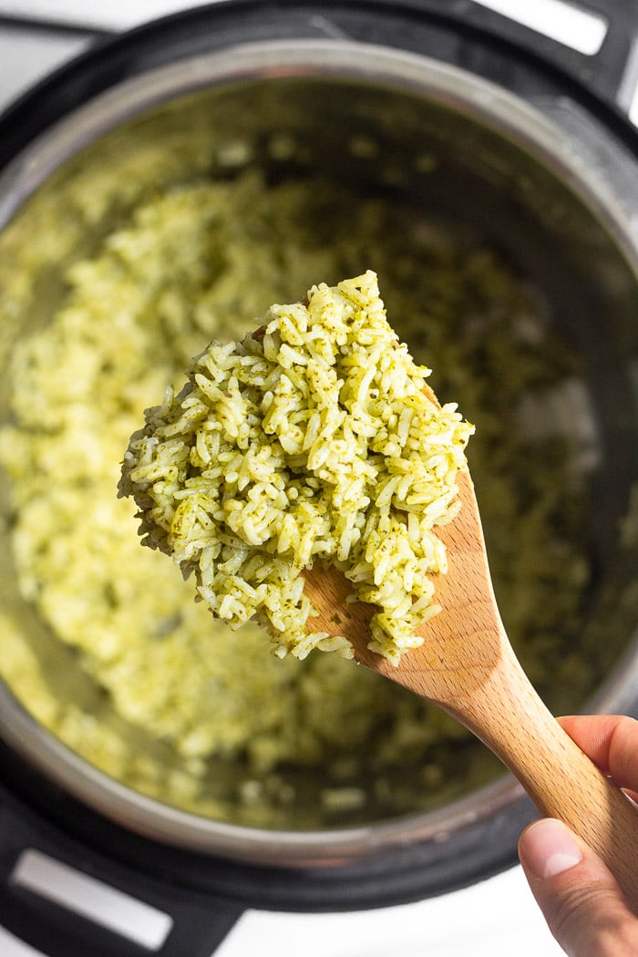 Overhead shot of scoop of instant pot pesto rice on a wooden spoon. Underneath it is the instant pot with more rice in it.