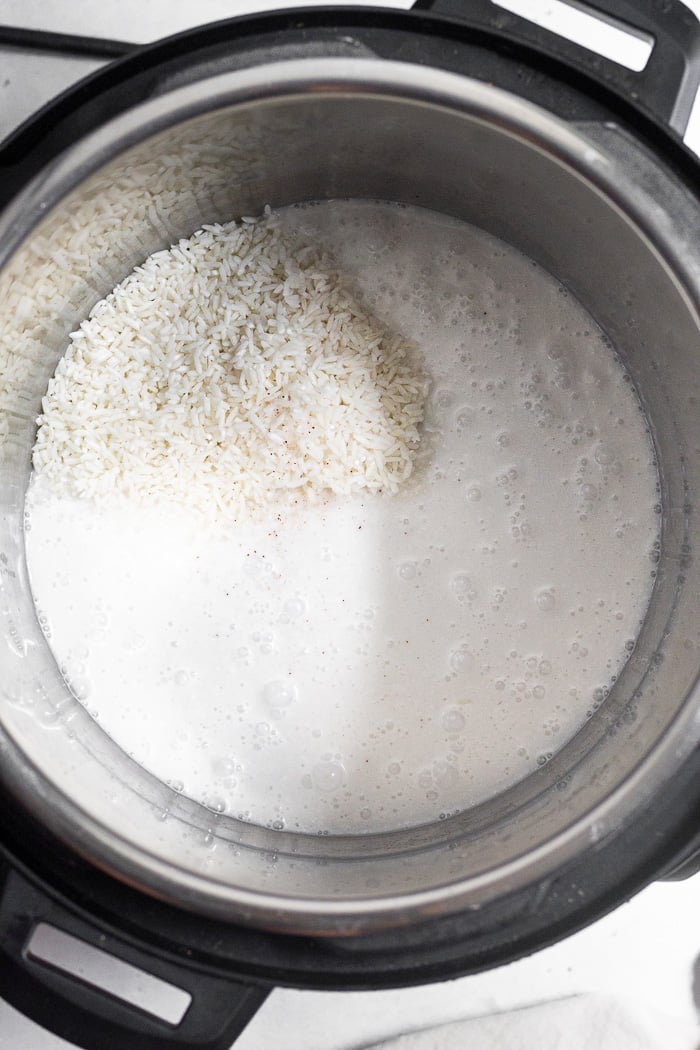 Instant pot bowl with uncooked white rice, coconut milk, and salt in it.