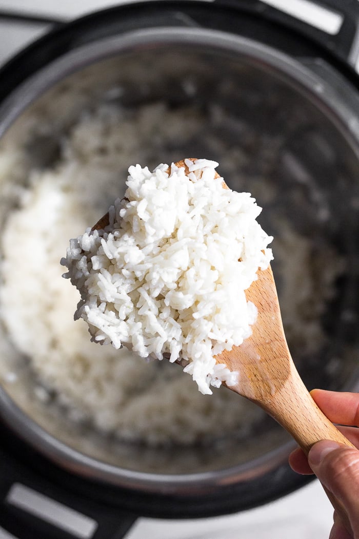 Overhead shot of scoop of instant pot coconut rice on a wooden spoon. Underneath it is the instant pot with more rice in it.