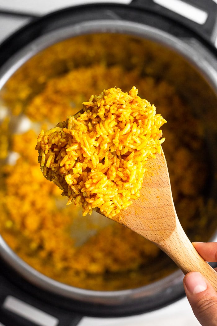 Overhead shot of scoop of instant pot curry rice on a wooden spoon. Underneath it is the instant pot with more rice in it.