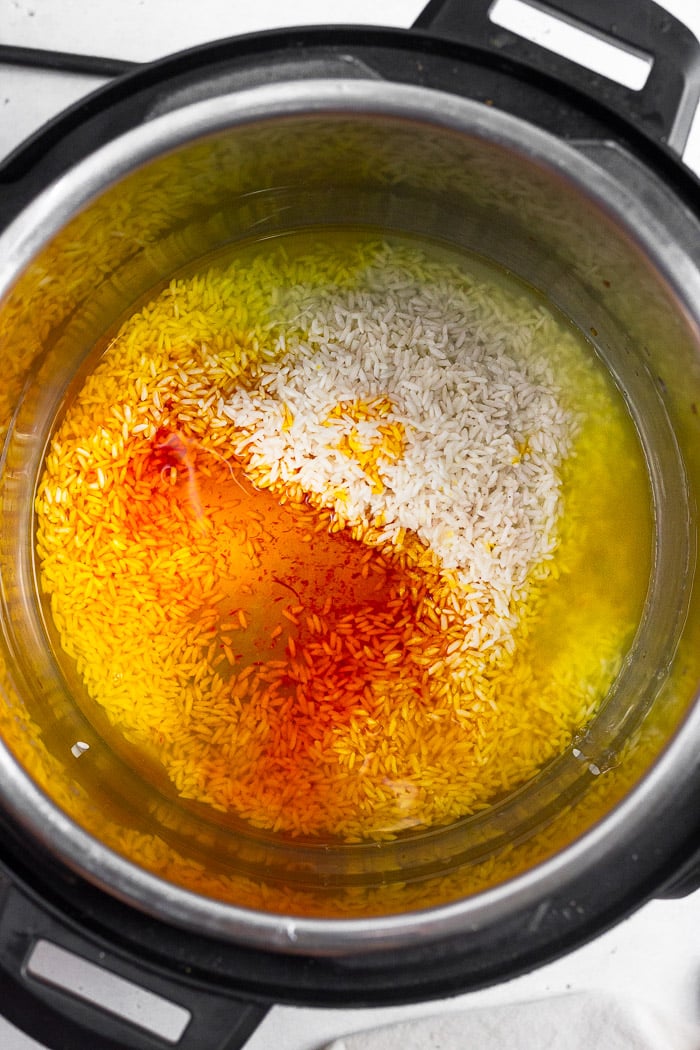 Instant pot bowl with uncooked white rice, saffron water, and salt in it.