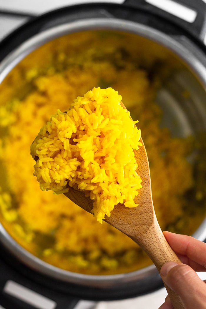 Overhead shot of scoop of instant pot saffron rice on a wooden spoon. Underneath it is the instant pot with more rice in it.