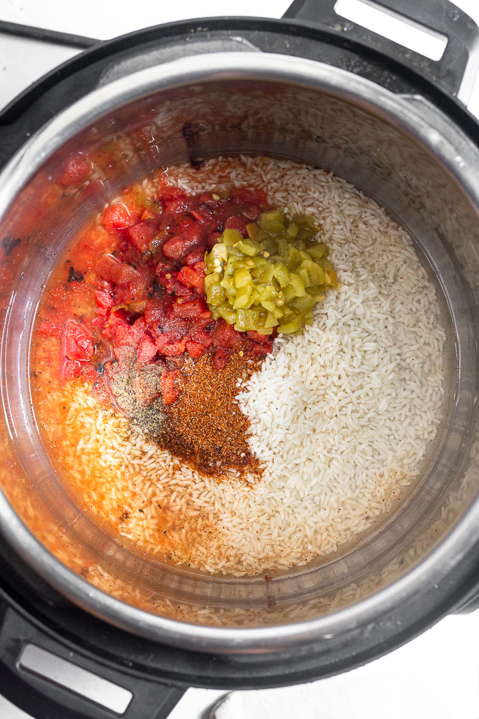 Instant pot bowl with uncooked white rice, water, canned fire-roasted tomatoes, canned green chilis, taco seasoning, and salt and pepper in it.