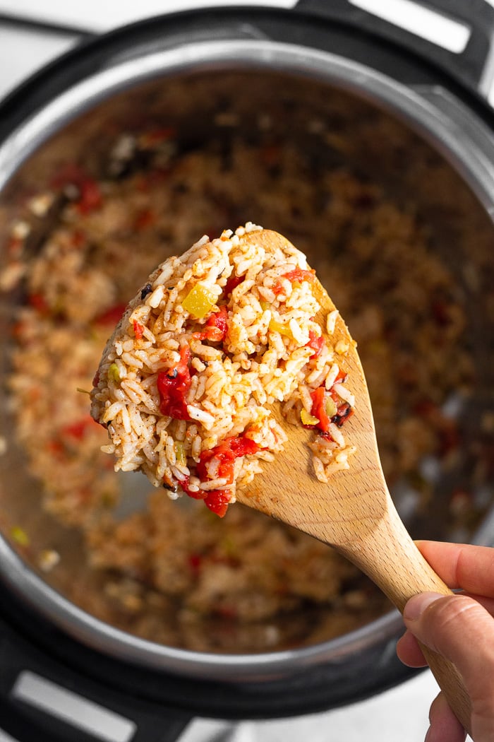 Overhead shot of scoop of instant pot Mexican rice on a wooden spoon. Underneath it is the instant pot with more rice in it.