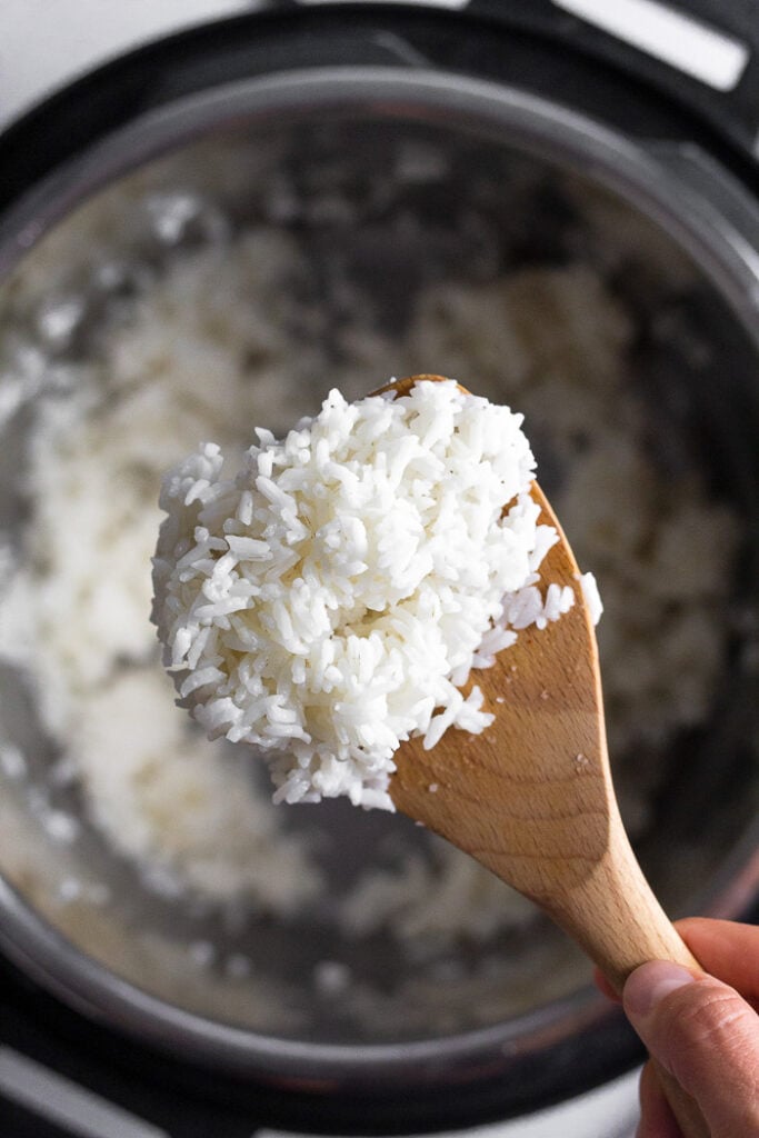 Overhead shot of scoop of instant pot white rice on a wooden spoon. Underneath it is the instant pot with more rice in it.