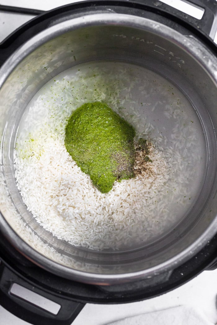 Instant pot bowl with uncooked white rice, water, pesto, and salt and pepper in it.