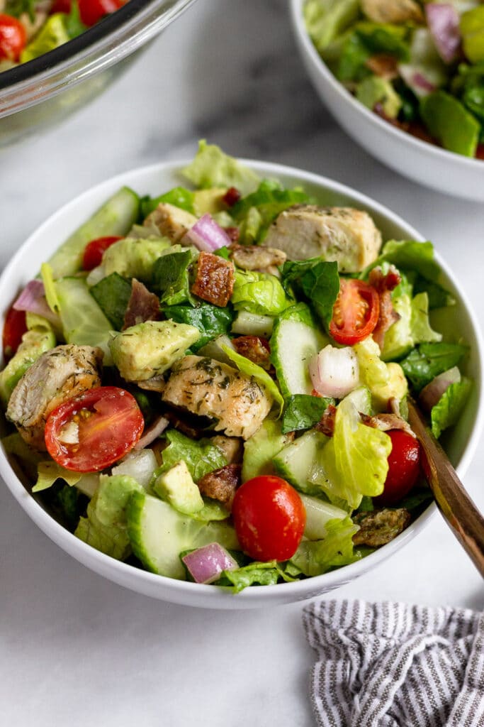 High protein chicken salad with lettuce, tomatoes, bacon, and avocado in a bowl. Around it is two more bowls of salad.