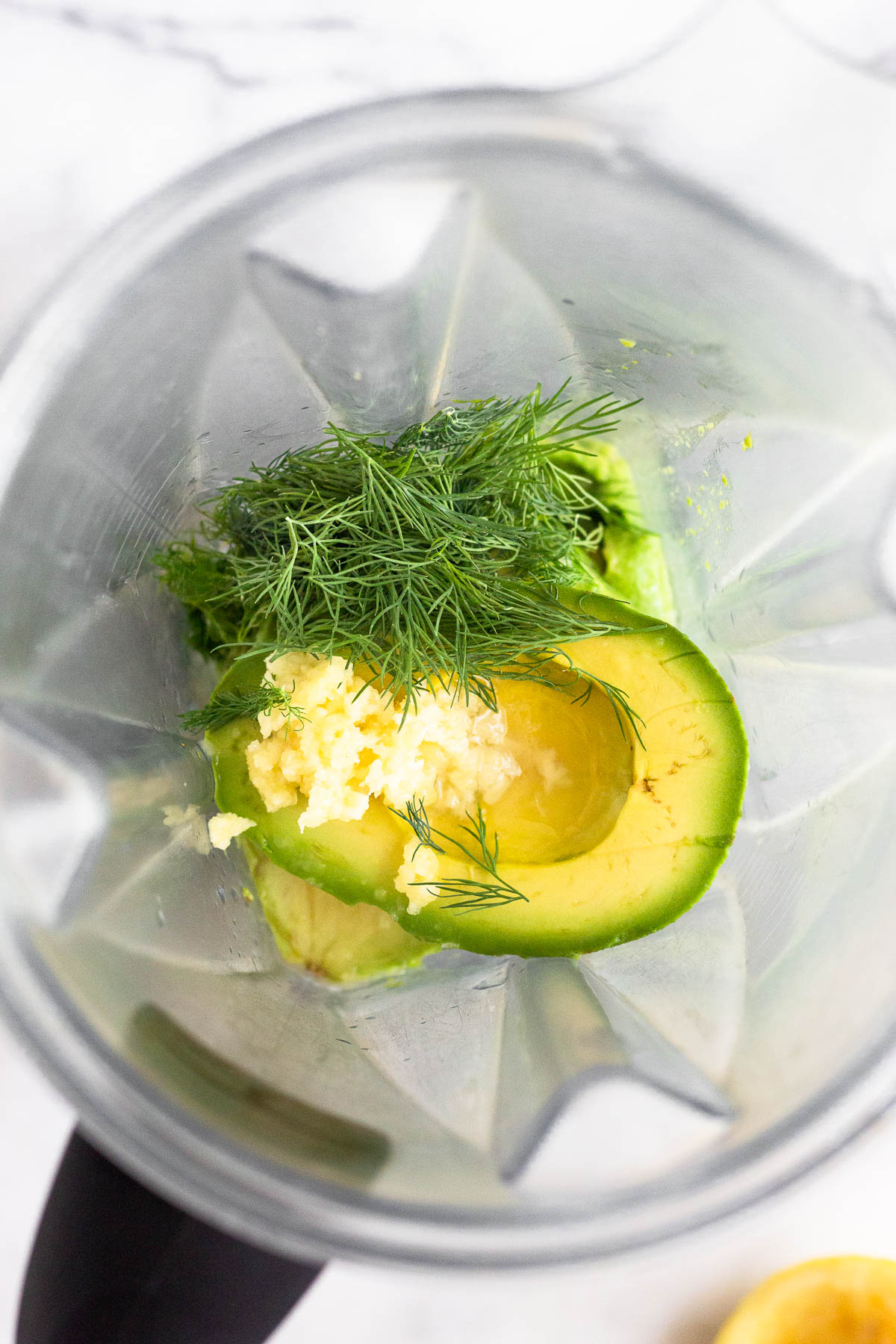 Blender filled with avocado, dill, and minced garlic.