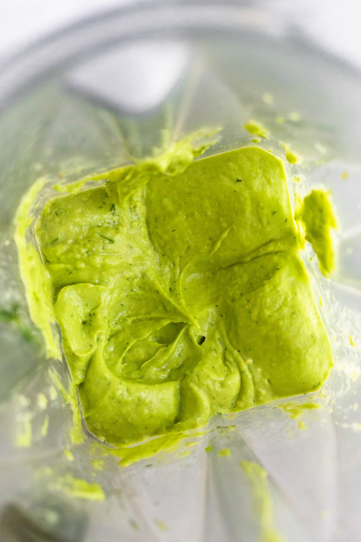 Blender filled with puréed avocado with some herbs.