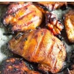 Close up of a grilled chicken thigh surrounded by more chicken thighs.