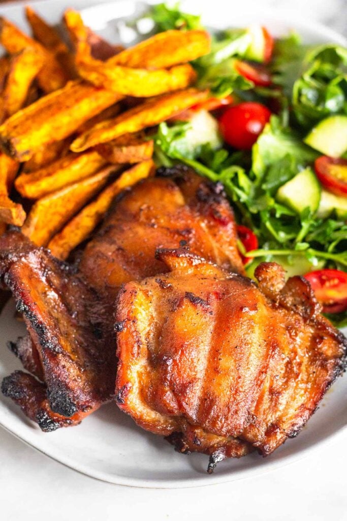 Plate of two grilled chicken thighs, sweet potato fries, and a salad.