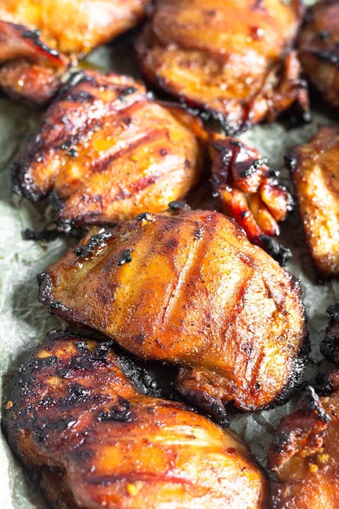 Close up of a grilled chicken thigh surrounded by more chicken thighs.