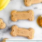 Overhead shot of peanut butter banana dog treats shaped as bones with a spoonful of peanut butter and bananas next to them.