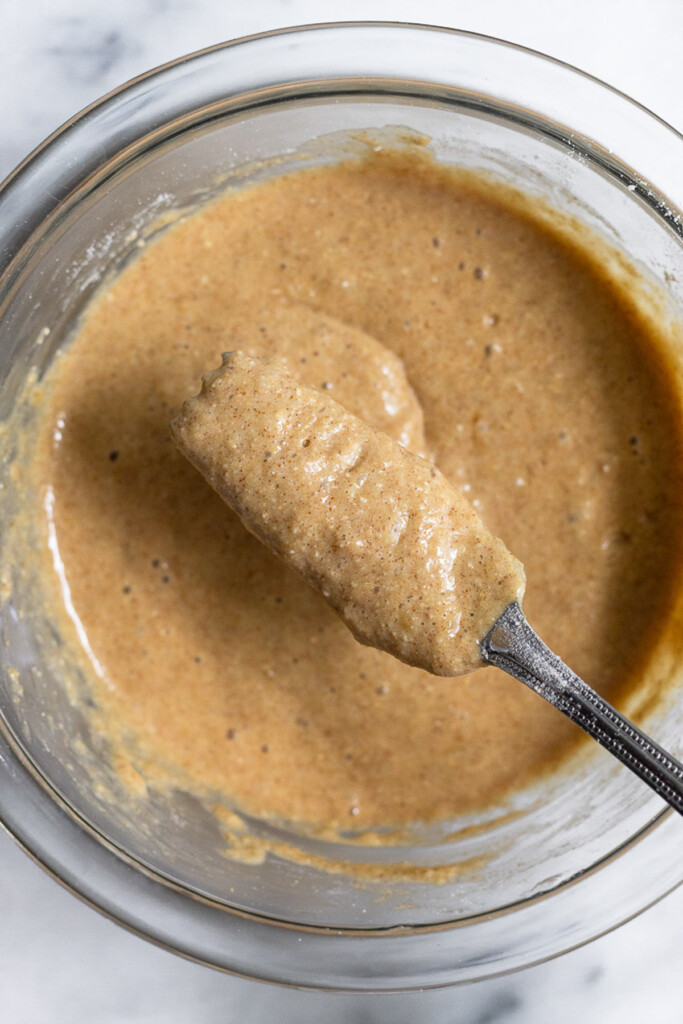 A glass bowl with pancake batter in it. A fork is overtop the bowl with some batter on it.