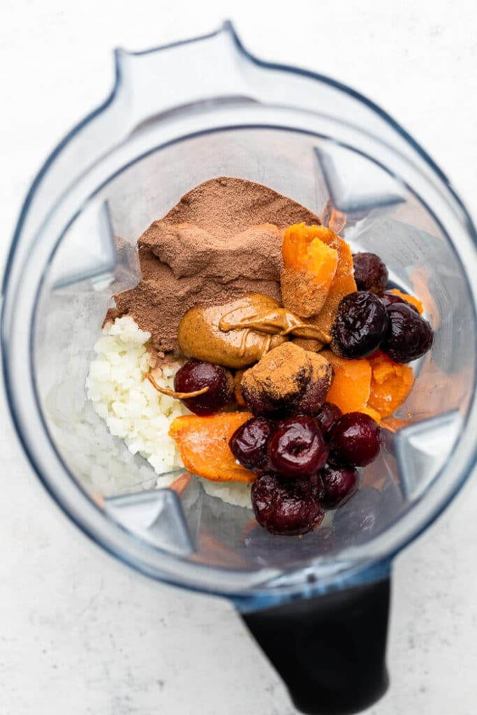 Blender filled with frozen fruit, frozen veggies, nut butter, and chocolate protein powder.