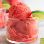 Watermelon sorbet in a small glass with a lime wedge. Next to it is a lime wedge and behind it is two more glasses.