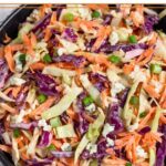 Blue cheese cole slaw in a black bowl sitting on a kitchen towel.