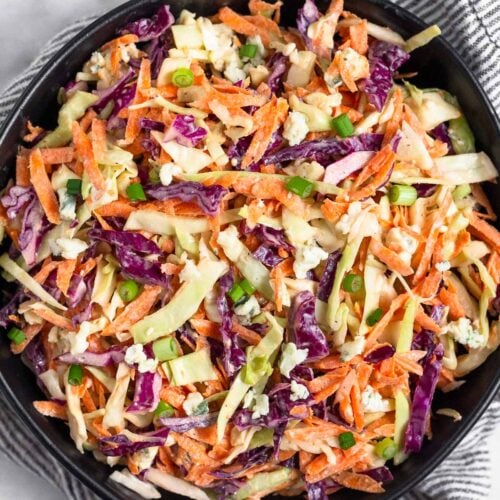 Overhead shot of blue cheese coleslaw in a black bowl. The bowl is on top of a kitchen towel and next to it a bowl of blue cheese.