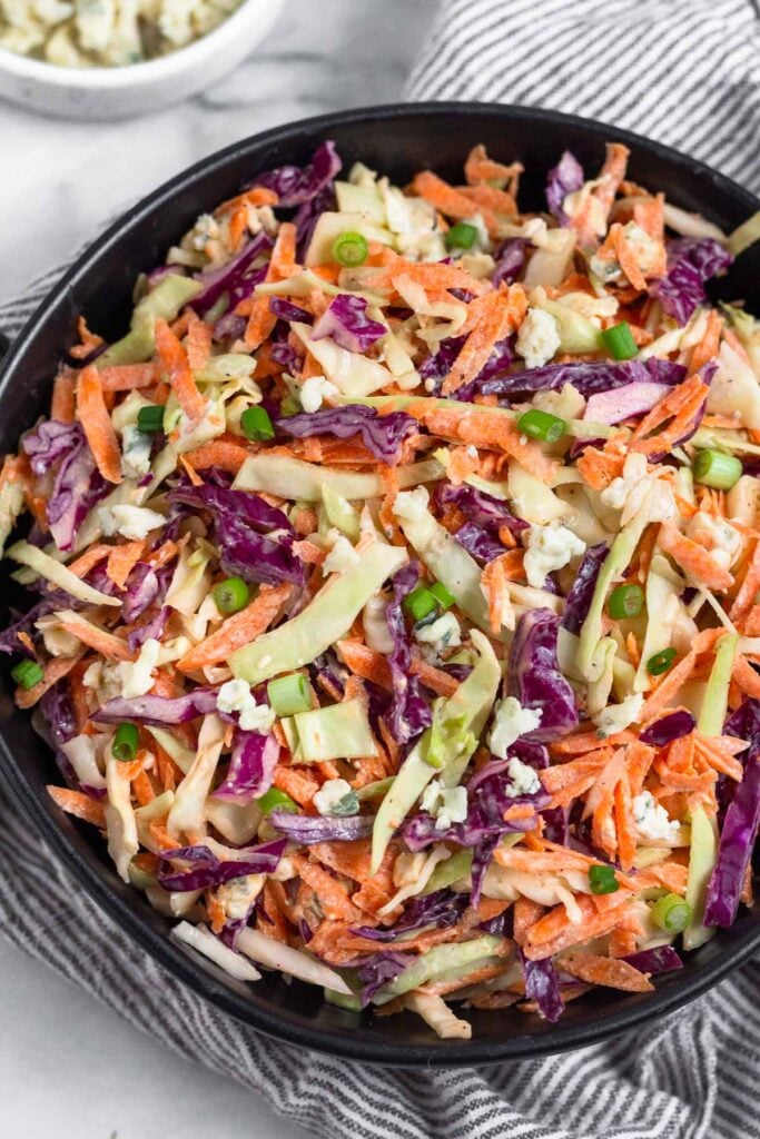 Blue cheese cole slaw in a black bowl sitting on a kitchen towel.