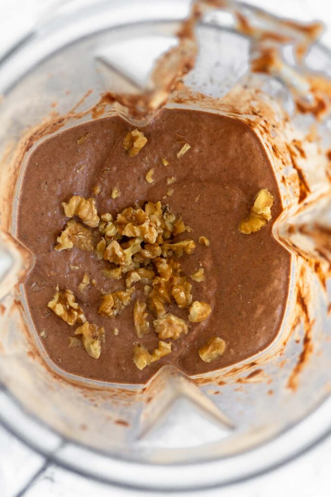 Overhead shot of a blender filled with a chocolate protein smoothie with walnuts sprinkled on top.