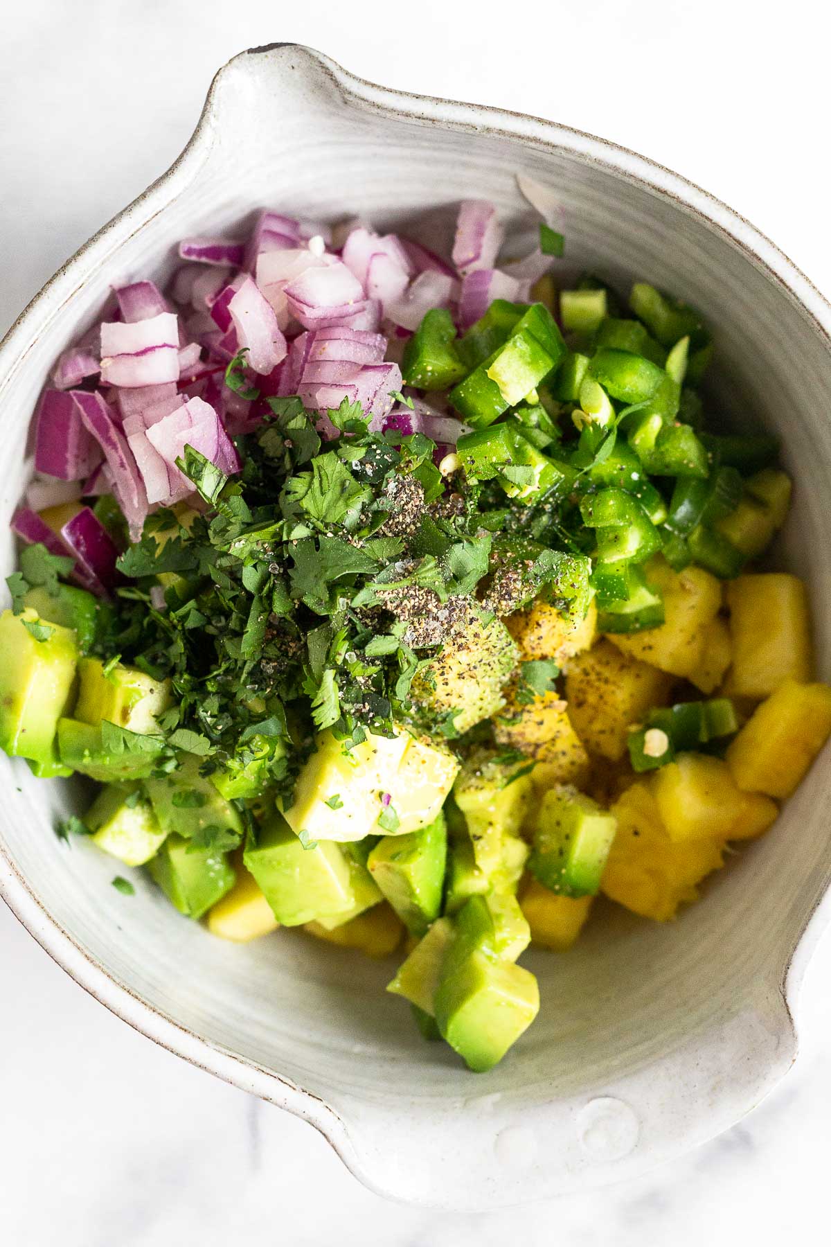 Bowl with diced pineapple, diced avocado, diced red onion, diced jalapeño, cilantro, and salt and pepper.