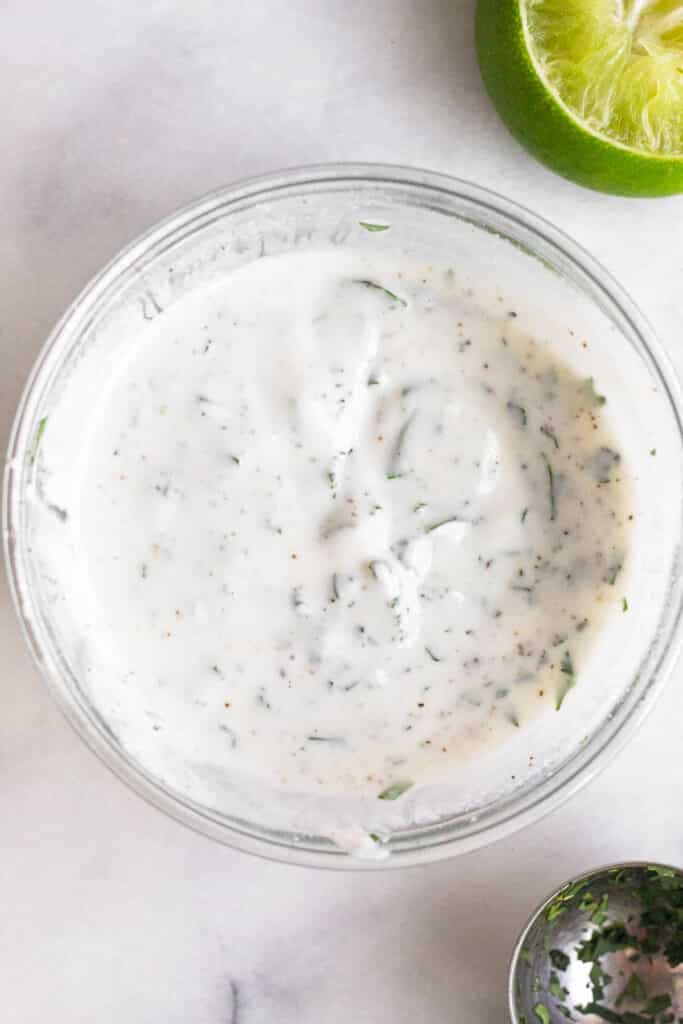 Fish taco sauce in a small glass bowl. Around it is a tablespoon and half a lime wedge.