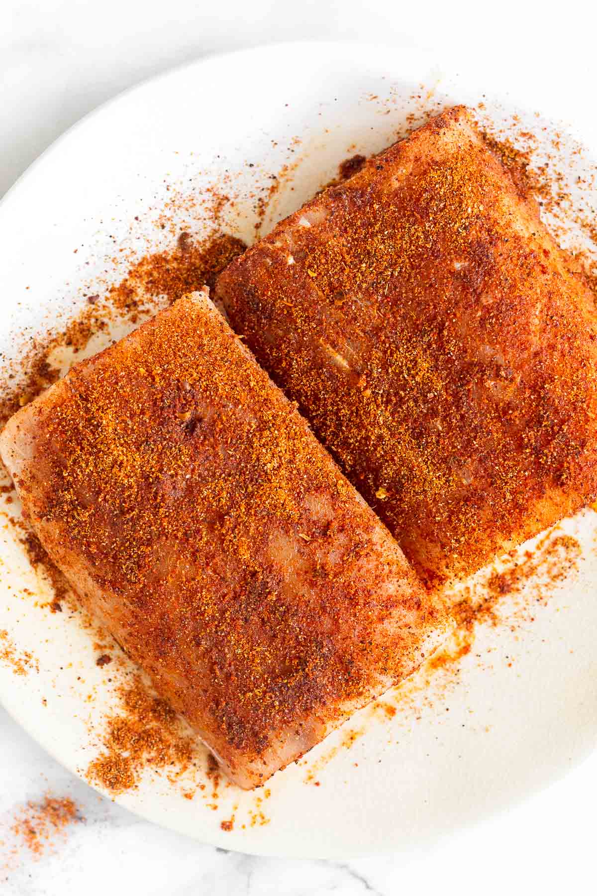 Two fillets of mahi mahi seasoned with taco seasoning on a white plate.