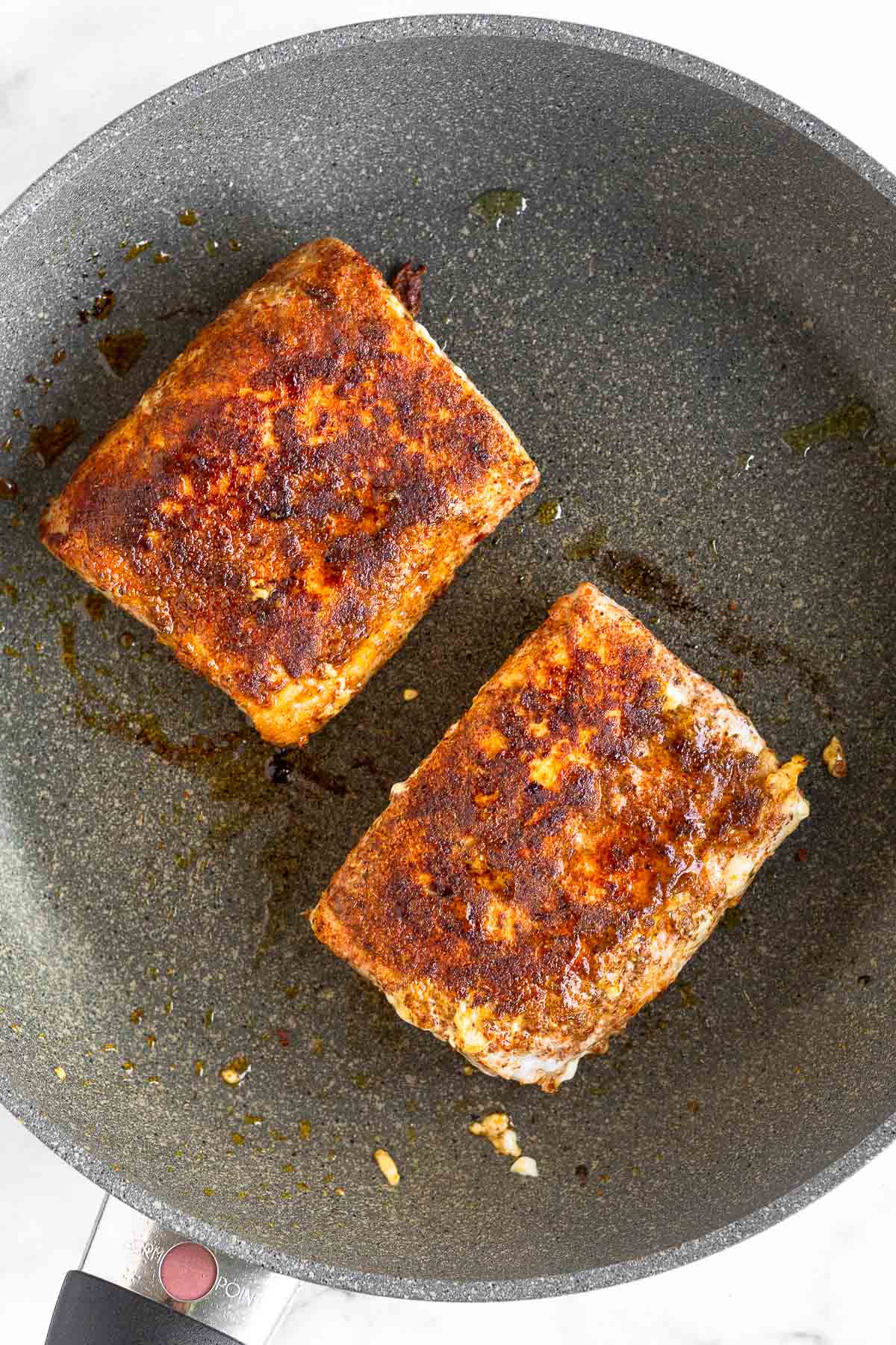 Two fillets of seasoned pan fried mahi mahi in a skillet.