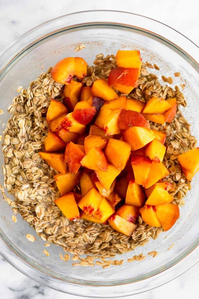 Glass bowl filled with on oatmeal mix with diced peaches on top of it.