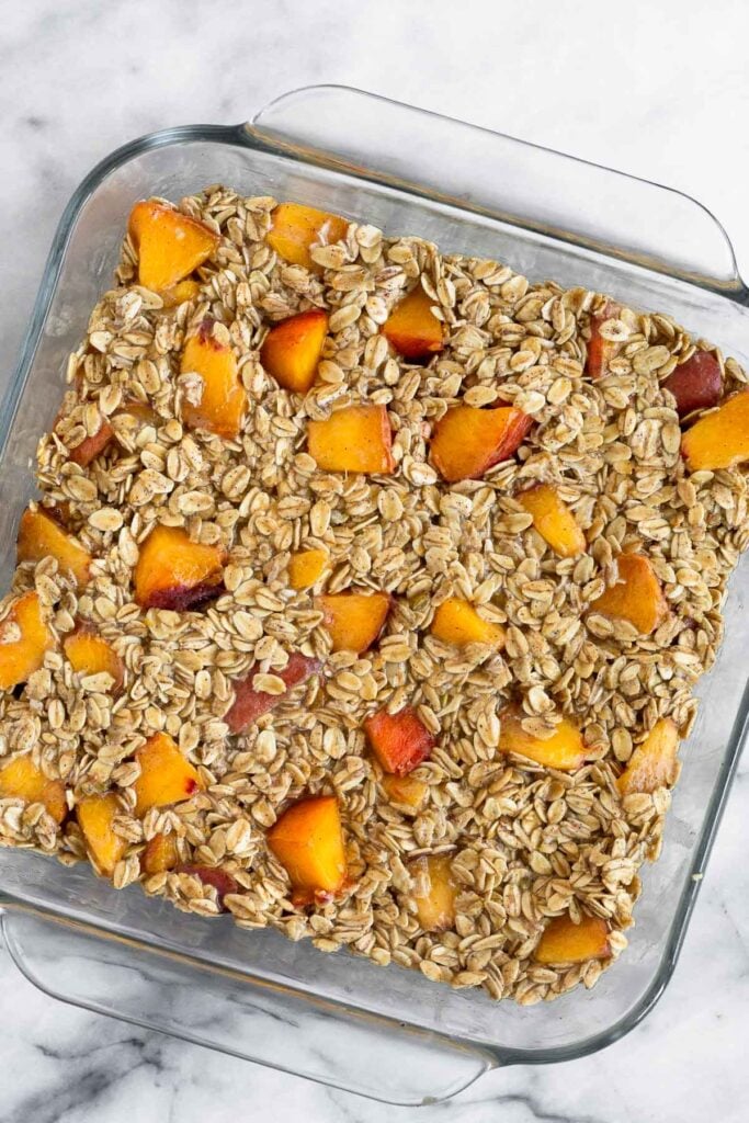 Baked oatmeal with peaches in a glass baking dish before it is baked.