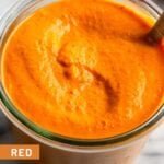 Jar filled with red pepper sauce with a spoon in it.