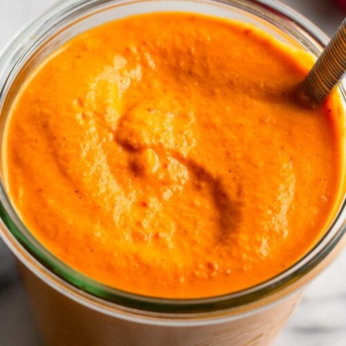 Jar filled with red pepper sauce with a spoon in it.
