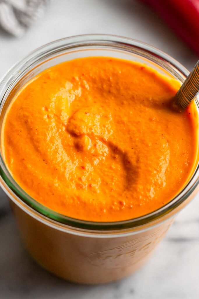 Jar filled with red pepper sauce with a spoon in it.