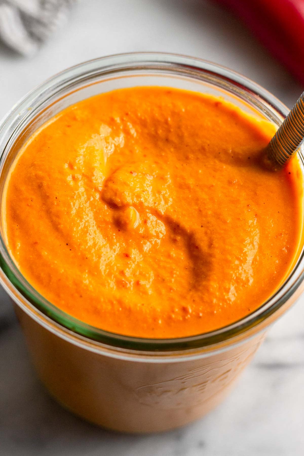 Jar filled with red pepper sauce with a spoon in it.