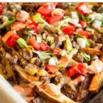 Close up of cheeseburger fries on a large baking sheet. The fries are topped with ground meat, melted cheese, lettuce, tomato, pickles, and special sauce.