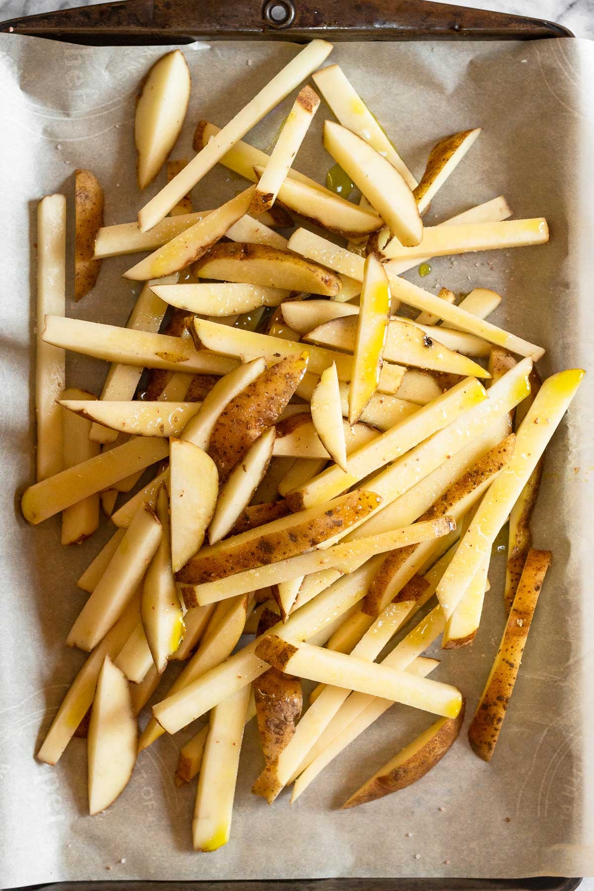 Overhead shot of uncooked french fries piled on a baking sheet lined with parchment paper.
