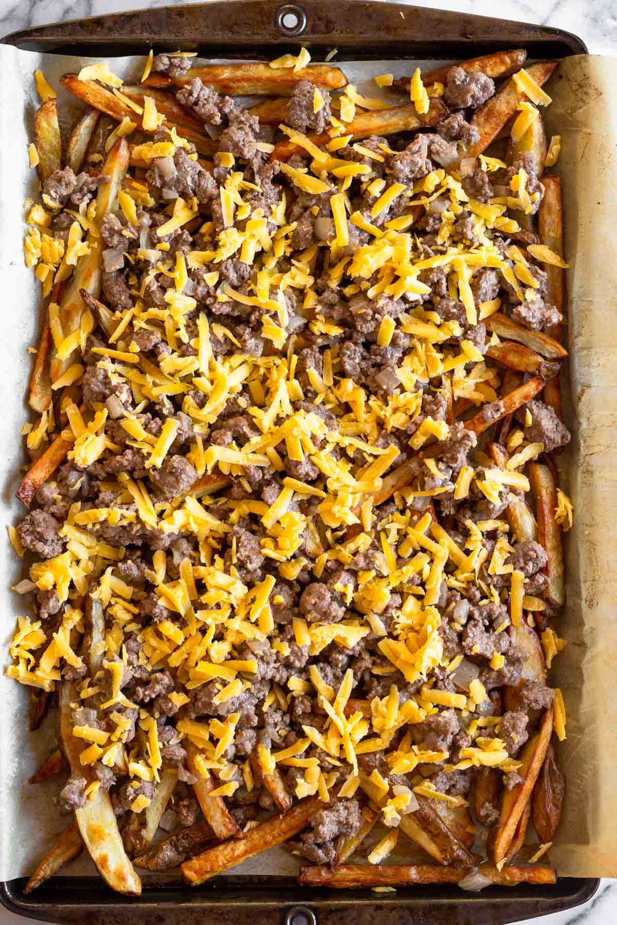 Large baking sheet of french fries topped with ground beef and shredded cheese.