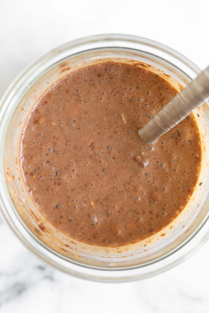Overhead shot of a jar filled with a mixture of milk, chocolate, rolled oats, and chia seeds.