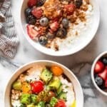 Overhead shot of two cottage cheese bowls. One is sweet with berries and granola and the is savory with veggies. Next to it a a kitchen towel, a bowl of berries, and a bowl of tomatoes.