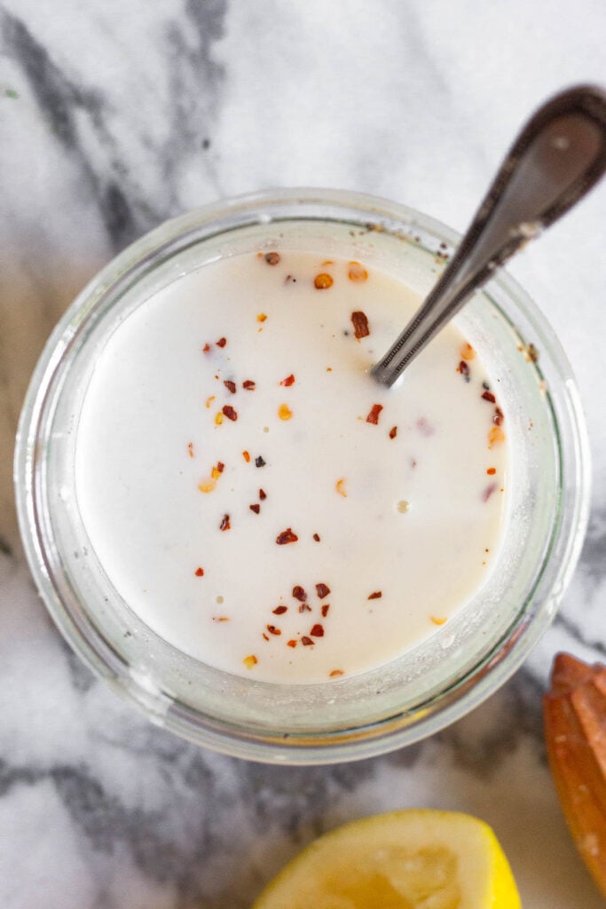 Jar filled with goat cheese pasta sauce with a spoon in it. Around it is half a lemon and a citrus reamer.