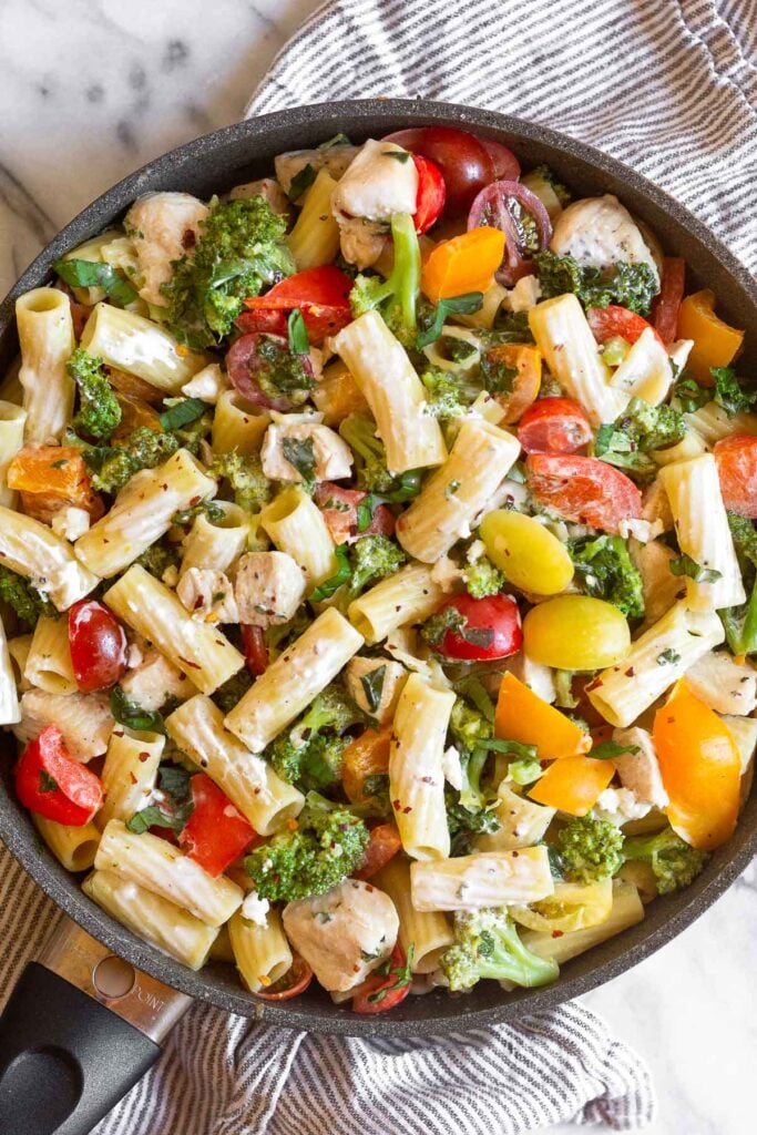 Goat cheese pastas with chicken and veggies in a large skillet stilling on a kitchen towel.