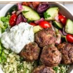 Overhead shot of a greek bowl with greek lamb meatballs, herby cauliflower rice, chopped romaine, greek salad, and tzatziki sauce.