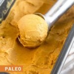 Bread pan filled with paleo pumpkin ice cream with an ice cream scoop filled with a scoop of pumpkin ice cream in it.