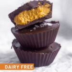 Three pumpkin pie chocolate cups on top of each other. The top one is cut in half with the other half next to the stack. A bowl of pumpkin pie butter is behind them
