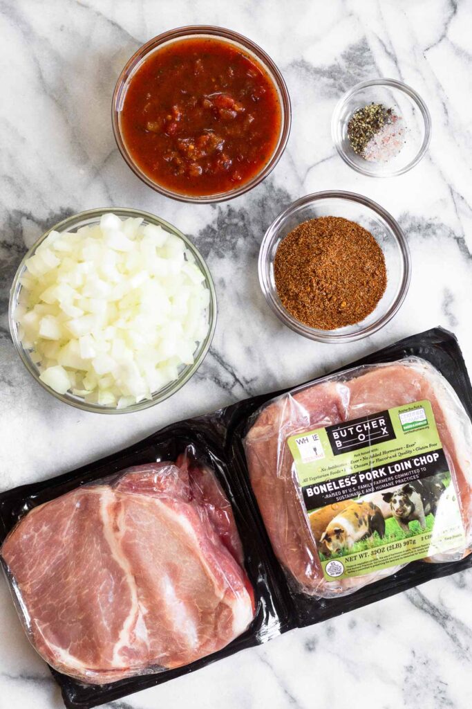 Marble countertop with a bowl of diced onion, bowl of salsa, bowl of salt and pepper, bowl of taco seasoning, and two packs of pork chops.