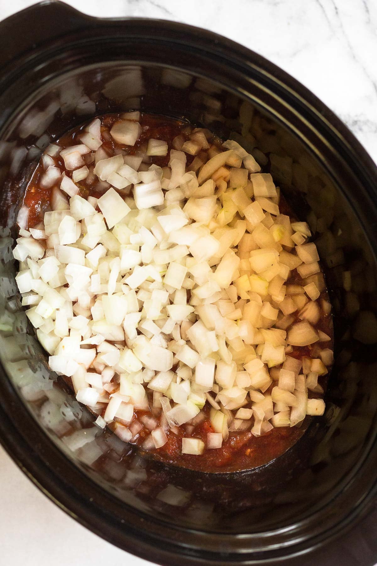 Overhead shot of a crockpot filled with salsa and diced onion.