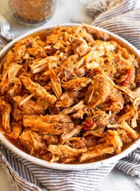 Shredded salsa pork chops on a plate sitting on a towel. Behind it is a jar of seasoning.