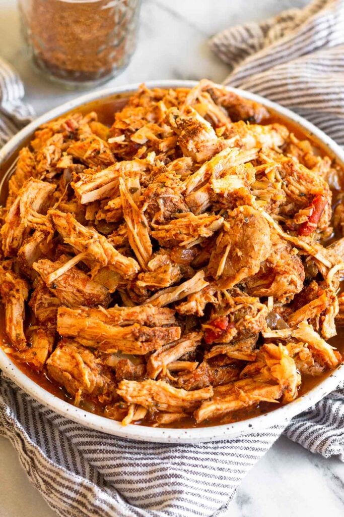 Shredded salsa pork chops on a plate sitting on a towel. Behind it is a jar of seasoning.