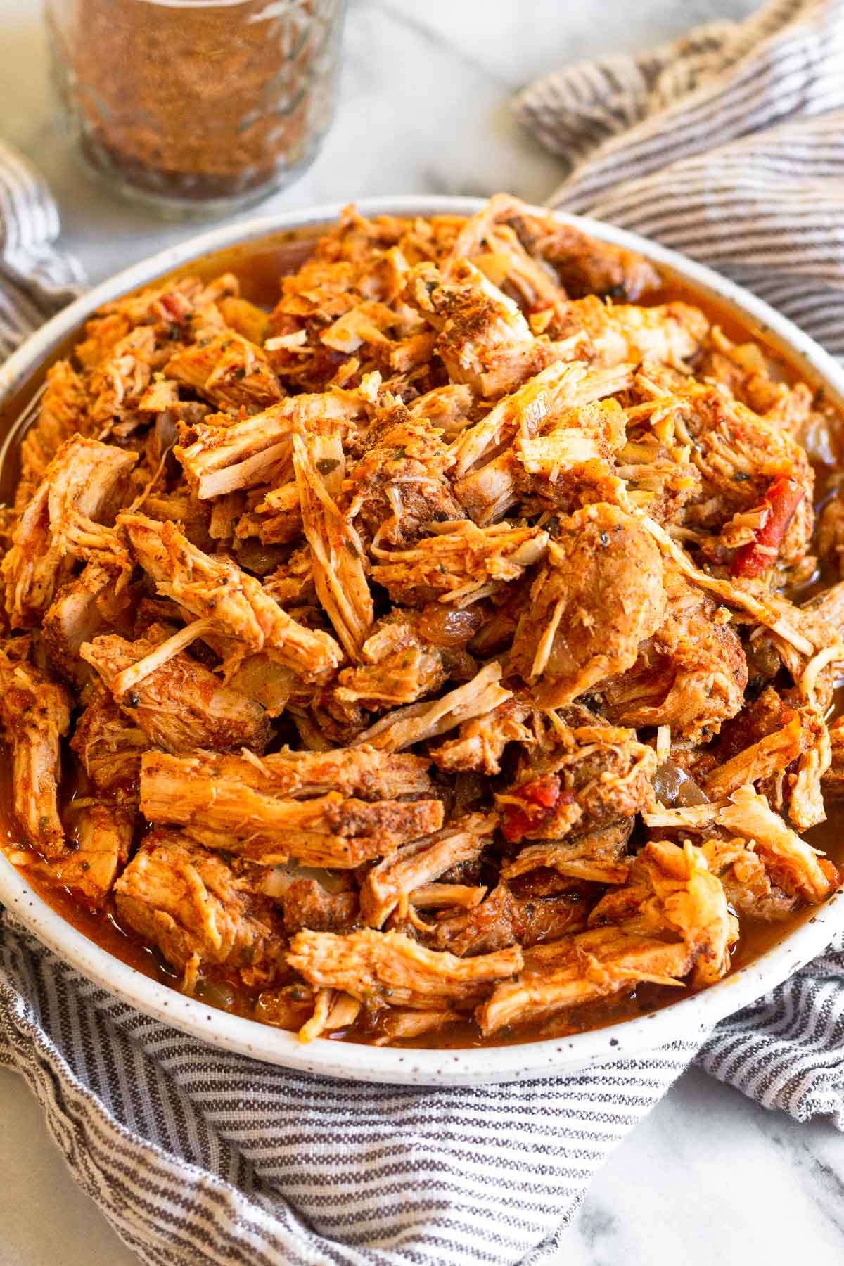 Shredded salsa pork chops on a plate sitting on a towel. Behind it is a jar of seasoning.